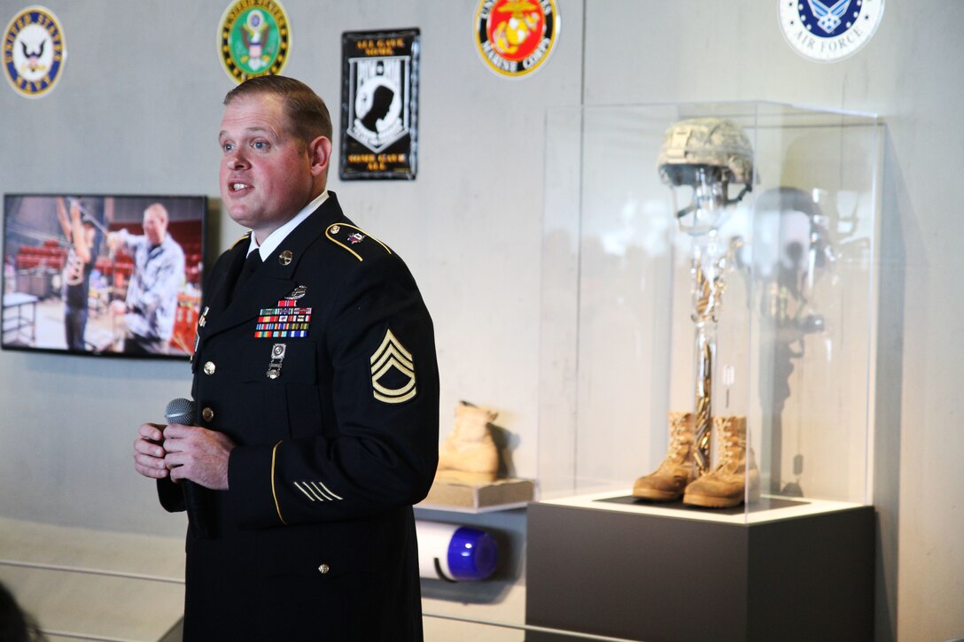 Sgt. 1st Class Peter Bazo from Ocala, Fla., with the Warrior Transition Battalion at Joint Base Lewis-McChord, Wash., explains the significance of "The Final Goodbye" (the piece behind him) at the Healing in Flames exhibition, Nov. 8, 2015, at the Museum of Glass in Tacoma, Wash. The Hot Shop Heroes program teaches soldiers glass art as a way to heal from the trauma of war. (U.S. Army photo by Pfc. Sarah K. Anwar)