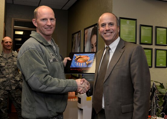 Jeff Greenlee, Altus community president, National Bank of Commerce Oklahoma, presents U.S. Air Force Col. Charles Ohliger, 97th Air Mobility Wing vice commander, with a book of paintings during the Mitten Tree kickoff, Nov. 17, 2015 at Altus Air Force Base, Okla. For the past nine years NBC has commissioned an Oklahoma artist to create a painting for the charitable event. (U.S. Air Force photo by Airman 1st Class Nathan Clark/Released)