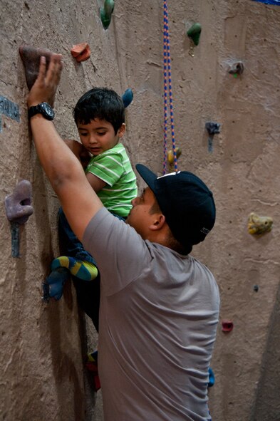 Staff Sgt. Marvin Reyes, 90th Civil Engineers Squadron locksmith, shows his son, Gabriel Reyes, 2, how to climb on a rock wall in the Fall Hall Community Center Nov. 19, 2015, during the base chapel’s Thanksgiving dinner event. The event was prepared with the combined effort of the chapel and the chapel community, which consist of people from the traditional, Catholic and contemporary services offered on base. (U.S. Air Force photo by Airman 1st Class Malcolm Mayfield)