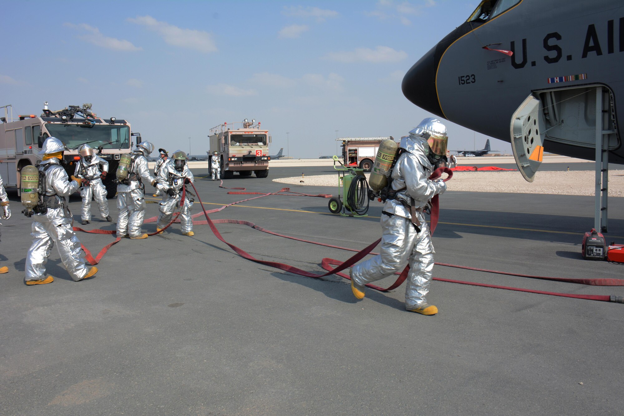 379th Civil Engineer Squadron firefighters work together to man several different fire hoses in an attempt to put out a simulated fire on a KC-135 Stratotanker and rescue an injured air crew member during a training exercise at Al Udeid Air Base, Qatar Nov. 20. Within minutes, several firefighters climbed on to the plane's left wing, entered the aircraft and pulled the injured air crew member to safety. Training exercises help first responders maintain their skillsets. (U.S. Air Force photo by Tech. Sgt. James Hodgman/Released)