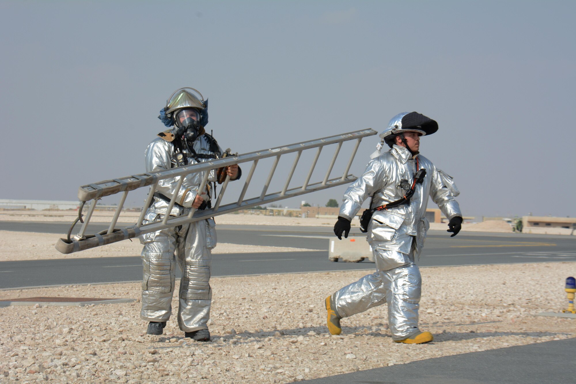 Two 379th Civil Engineer Squadron firefighters, one carrying a ladder, respond to a training exercise at Al Udeid Air Base, Qatar Nov. 20. The ladder was needed to gain access to a KC-135 Stratotanker to rescue a injured air crew member from the cockpit. Training exercises help first responders maintain their skillsets. (U.S. Air Force photo by Tech. Sgt. James Hodgman/Released)