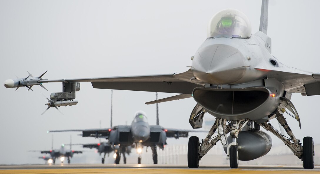 An F-16 Fighting Falcon from the 8th Fighter Wing is parked at the end of the runway as Republic of Korea air force F-15K Slam Eagles from the 11th Fighter Wing, Daegu, taxi behind it during Buddy Wing 15-7 at Kunsan Air Base, Republic of Korea, Nov. 17, 2015. Buddy Wing exercises are held multiple times a year to not only enhance interoperability between the USAF and ROKAF combat Airmen, but to promote cultural awareness through operating as one force as they integrated mission planning, briefing, flying and debriefing together. (U.S. Air Force photo by Staff Sgt. Nick Wilson/Released)