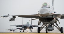 An F-16 Fighting Falcon from the 8th Fighter Wing is parked at the end of the runway as Republic of Korea air force F-15K Slam Eagles from the 11th Fighter Wing, Daegu, taxi behind it during Buddy Wing 15-7 at Kunsan Air Base, Republic of Korea, Nov. 17, 2015. Buddy Wing exercises are held multiple times a year to not only enhance interoperability between the USAF and ROKAF combat Airmen, but to promote cultural awareness through operating as one force as they integrated mission planning, briefing, flying and debriefing together. (U.S. Air Force photo by Staff Sgt. Nick Wilson/Released)