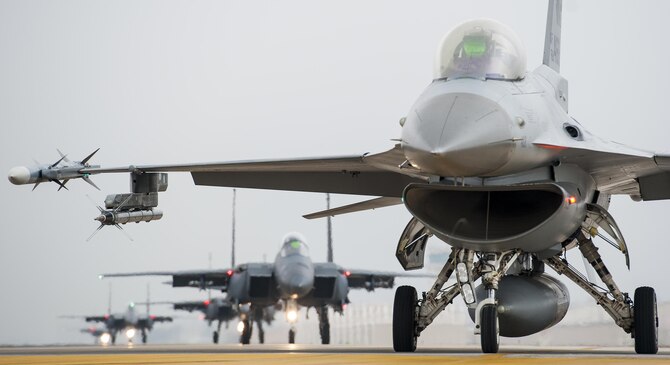 An F-16 Fighting Falcon from the 8th Fighter Wing is parked at the end of the runway as Republic of Korea air force F-15K Slam Eagles from the 11th Fighter Wing, Daegu, taxi behind it during Buddy Wing 15-7 at Kunsan Air Base, Republic of Korea, Nov. 17, 2015. Buddy Wing exercises are held multiple times a year to not only enhance interoperability between the USAF and ROKAF combat Airmen, but to promote cultural awareness through operating as one force as they integrated mission planning, briefing, flying and debriefing together. (U.S. Air Force photo by Staff Sgt. Nick Wilson/Released)