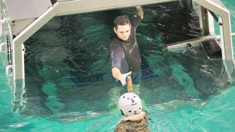 An underwater trainer instructor with the Water Survival Training Facility helps a Marine with 2nd Low Altitude Air Defense Battalion into the modular amphibious egress mock helicopter, at Marine Corps Base Camp Lejeune, N.C., Nov. 18, 2015. The Marines participated in the training, which is designed to be a lifesaving course that provides service members with skills and the confidence to successfully and safely exit a helicopter that is submerged in a body of water.