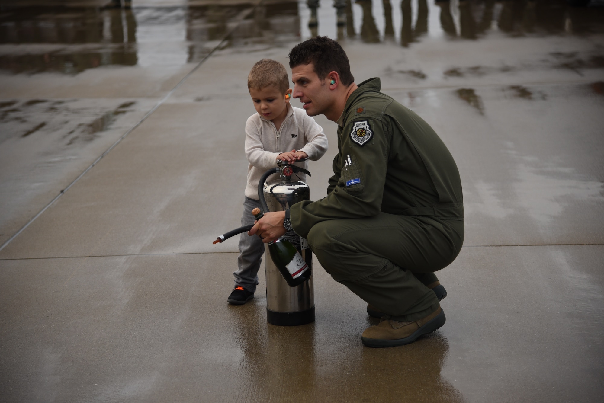 U.S. Air Force Maj. Kiel Gilliland waits with his son, Garrett below a KC-135R Stratotanker piloted by his wife, U.S. Air Force Maj. Sharon Gilliland at Joint Base Mcguire-Dix-Lakehurst on Nov, 5 2015. Sharon Gilliland’s mid-air refueling was specially coordinated between her Air National Guard and his Air Force Reserve units to celebrate her final flight, also called a “fini flight” aboard to KC-135. Gilliland, a pilot for 12 years with the New Jersey Air National Guard’s 108th Wing is ceremonially hosed down by fellow pilots, crewmembers, friends and family as she leaves piloting to others and takes a non-flying job with the 514th AMOS, Air Force Reserve so she can devote more time to her family. During her time in the 108th Wing, Gilliland deployed three times and has 60 combat sorties to her credit. (U.S. Air National Guard photo by Master Sgt. Carl Clegg/Released)  
