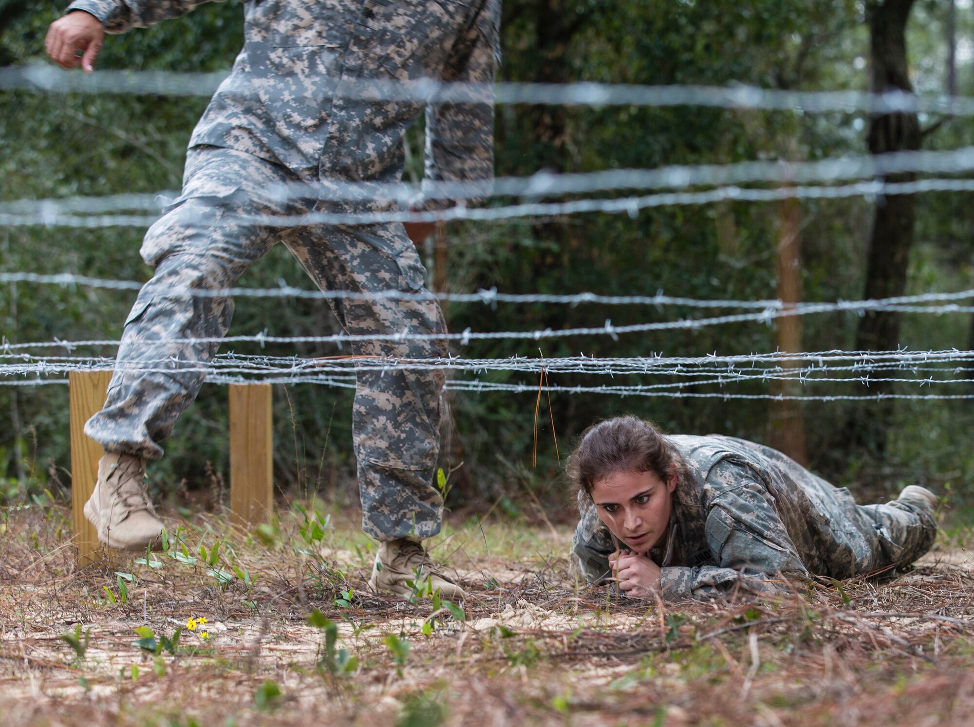 An Army Junior Officer Training Corps Cadet low-crawls underneath a barbed wire obstacle on the 7th Special Forces (Airborne) compound Nov. 10 while under the observation of a soldier assigned to the group. The Army JROTC cadet and others from Baker School in Northwest Florida trained with Special Forces soldiers from the group to prepare for an upcoming competition testing their physical and mental endurance. (U.S. Army photo/Pfc David Stewart)