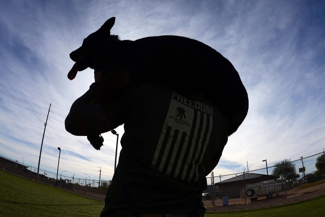 Air Force Staff Sgt. Justin Gonzalez carries military working dog Rango on Luke Air Force Base, Ariz., Nov. 18, 2015. Gonzalez is a military working dog handler with the 56th Security Forces Squadron. Military dog handlers train to make sure they can carry both a full ruck sack and their dog in the event of an injury or if the dog becomes too tired to move. U.S. Air Force photo by Senior Airman James Hensley