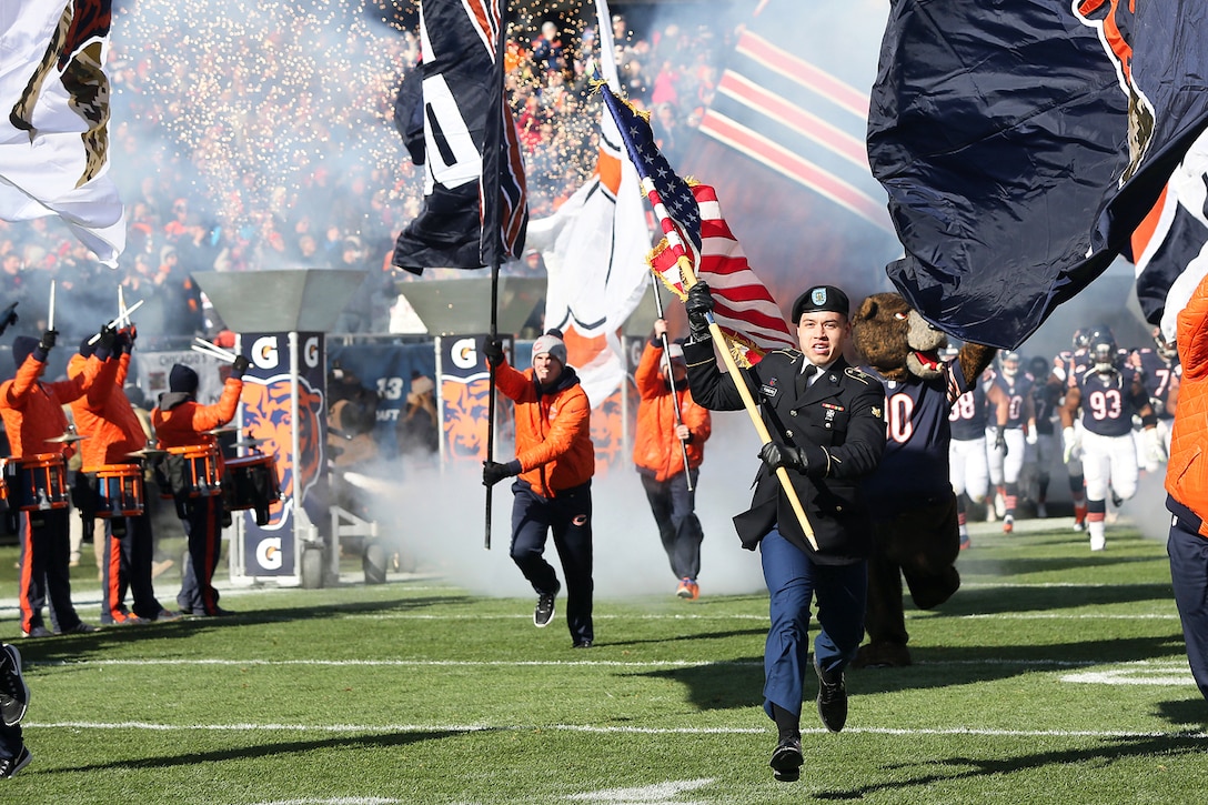 Army Spc. Leopoldo Guerrero leads the Chicago Bears onto Soldier Field at the start of the Bears game against the Denver Broncos in Chicago, Nov. 22, 2015. More than 100 service members participated in game-day activities honoring veterans at the stadium. Guerrero is assigned to the 814th Military Police Company.