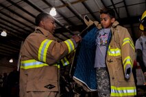 U.S. Air Force Airman 1st Class Christopher Walker, a 509th Civil Engineer Squadron firefighter, helps Nakai, the son of Tech. Sgt. David Brandon, the 509th Medical Operations Squadron mental health flight chief, try on protective gear during Operation Spirit at Whiteman Air Force Base, Mo., Nov. 21, 2015. Walker and other firefighters showed children how they help keep Airmen safe during deployments. (U.S. Air Force photo by Senior Airman Sandra Marrero)