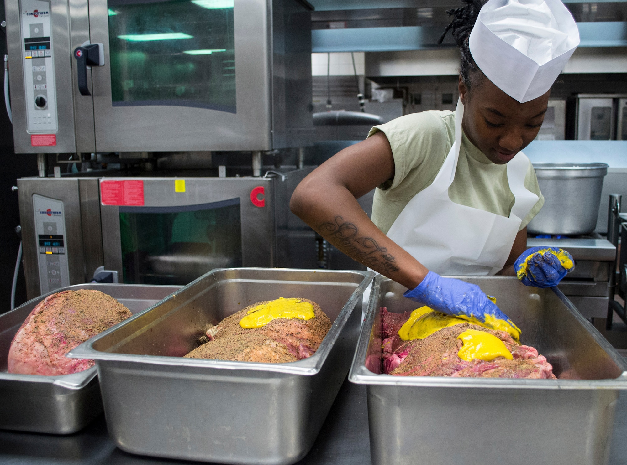 A culinary specialist assigned to the 7th Special Forces Group (Airborne) spreads mustard over steamship round roasts as she and others prepare a Thanksgiving meal in the unit’s dining facility November 23.  The group’s culinary specialist team prepared over 600 pounds of turkey, 115 pounds of steamship round and 184 pounds of ham for serving to the group’s soldiers, families and friends. (U.S. Army photo/Maj. Thomas Cieslak)