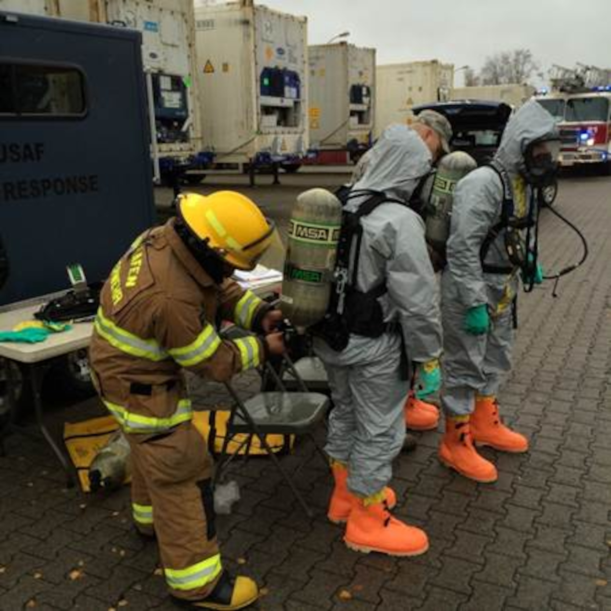 Firefighters from the 86th Civil Engineering Squadron suit up in hazmat suits as they prepare to quell a chemical line rupture Nov. 17, 2015, at Ramstein Air Base, Germany. The rupture spewed hazardous chemicals within a cold storage facility containing Defense Commissary Agency food items. (Courtesy photo)