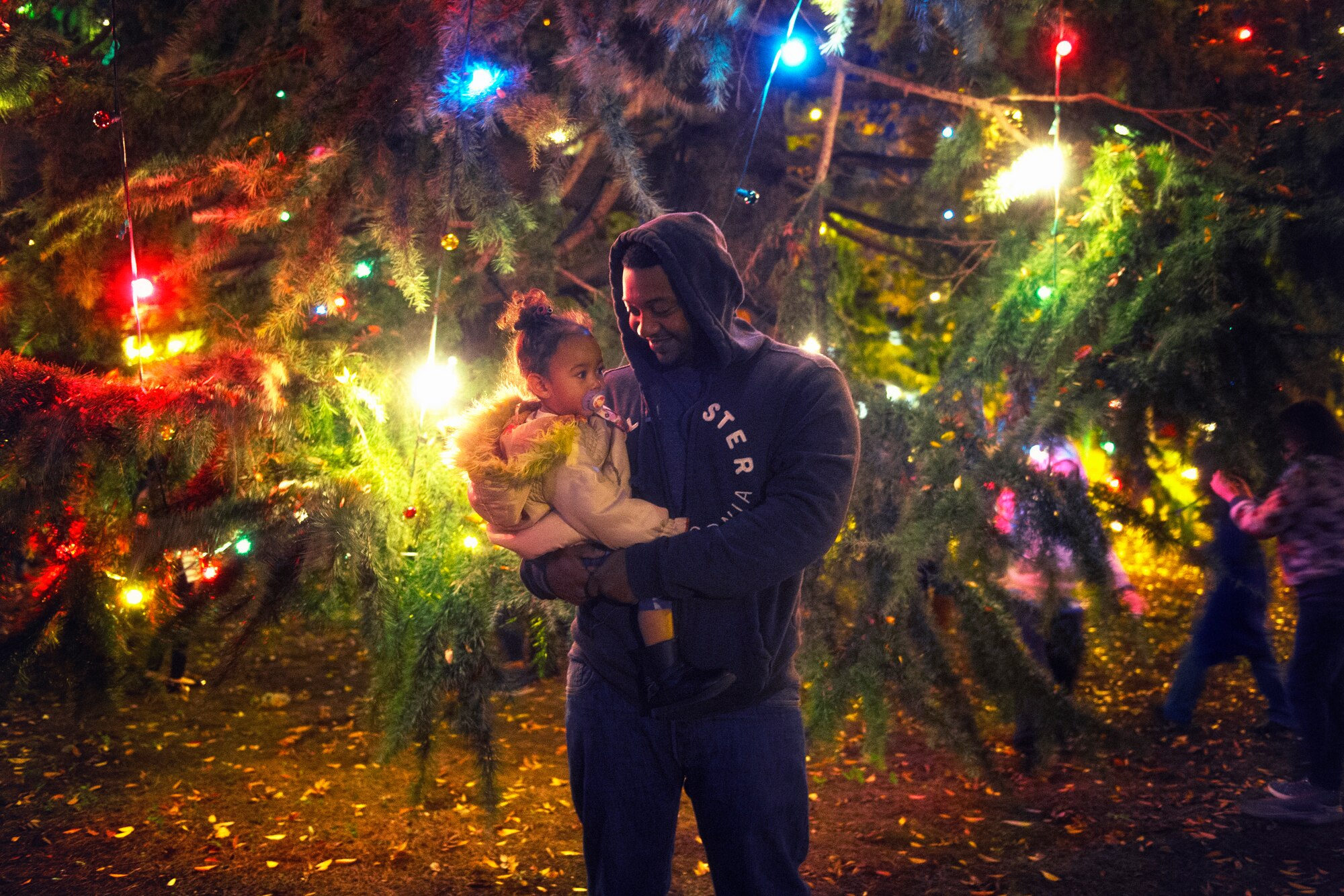 Staff Sgt. Andre Hayes, 374th Civil Engineer Squadron journeyman, holds his daughter during the holiday tree lighting ceremony at Yokota Air Base, Japan, Nov. 24, 2015. The lighting of the tree signals the beginning of the holiday season. (U.S. Air Force phot by Airman 1st Class Delano Scott/Released)