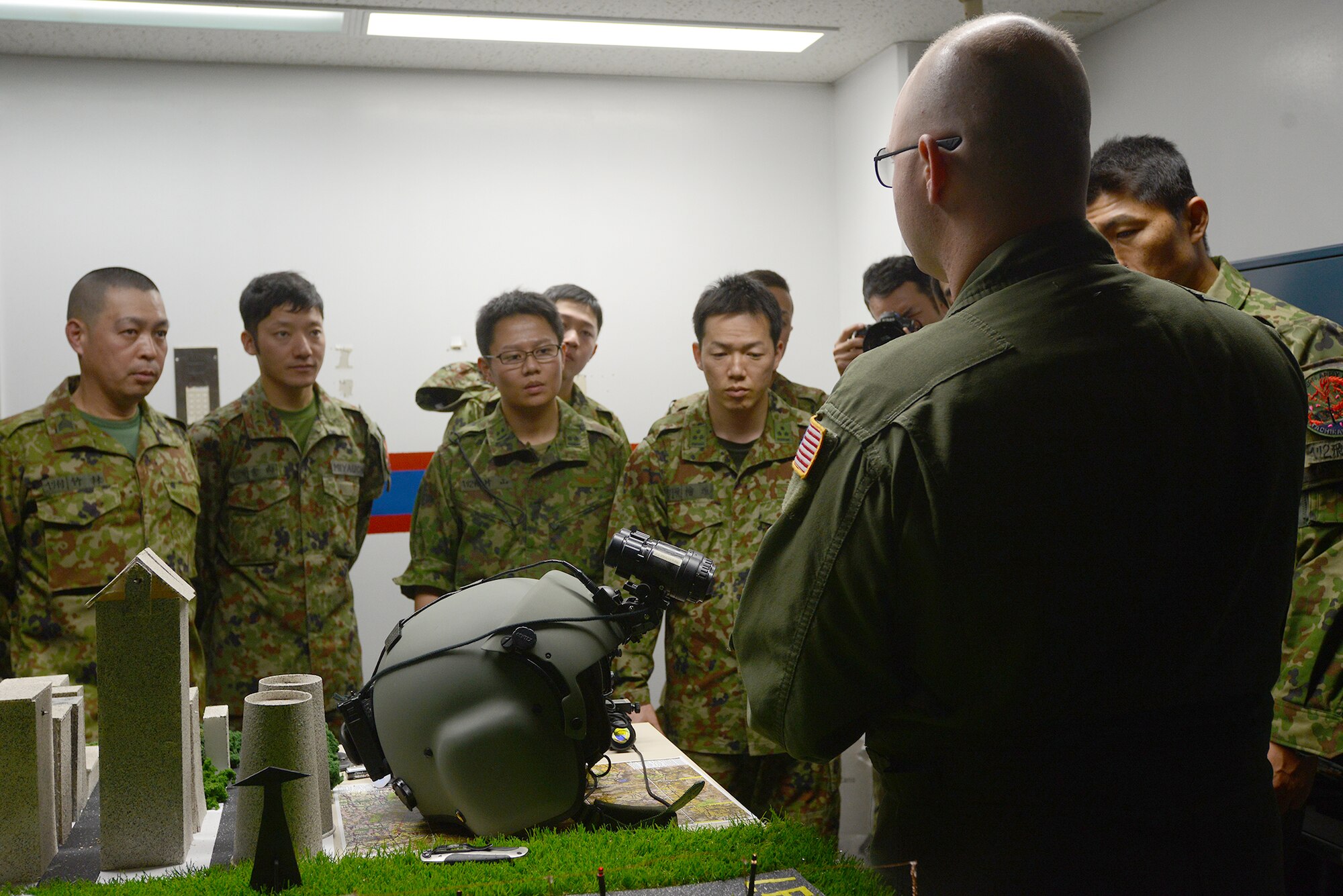 Tech. Sgt. Christopher Rector, 459th Airlift Squadron UH-1N Iroquois standards and evaluations NCO in charge, briefs a Japan Ground Self-Defense Force helicopter aircrew on night vision search and rescue capabilities at Yokota Air Base, Japan, Nov. 16, 2015. JGSDF members were then given the opportunity to experience the night vision goggles while the diorama simulated the view from a helicopter. (U.S. Air Force photo by Senior Airman David C. Danford/Released)