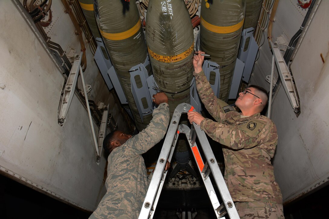 Service members write messages on a bomb inside one of the B-1 Lancer bomb bays during a tour of the aircraft at Al Udeid Air Base, Qatar Nov. 24. Forty service members took part in the tour which featured a presentation of the B-1's capabilities and videos showcasing strikes the bomber has carried out. (U.S. Air Force photo by Tech. Sgt. James Hodgman/Released)