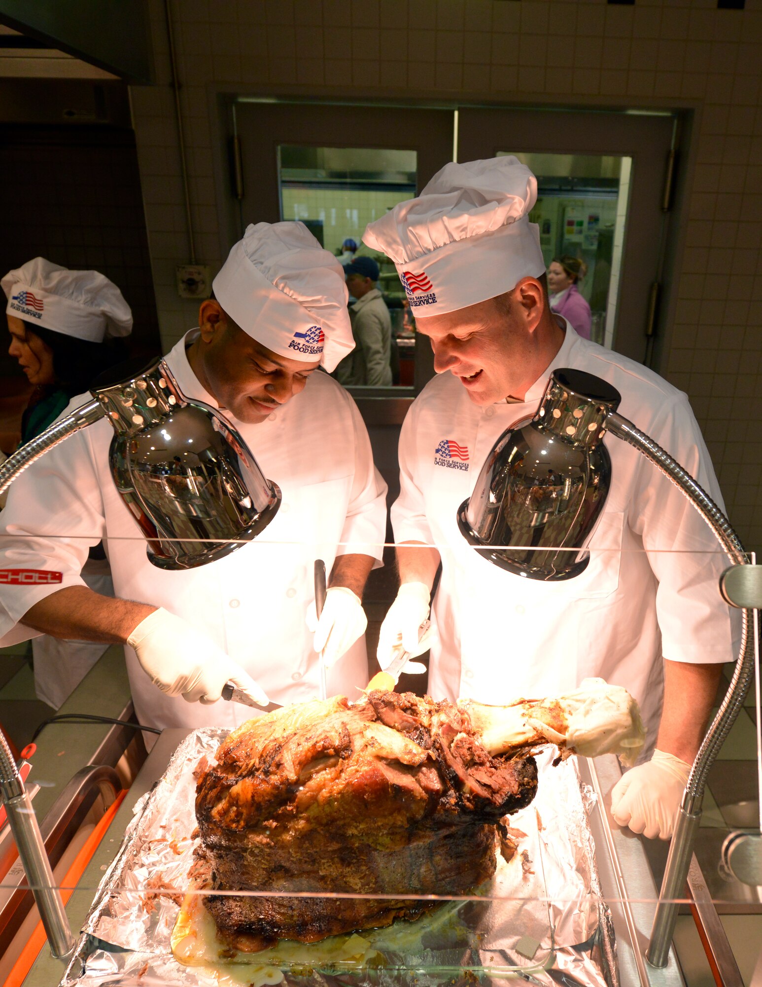 Brig. Gen. Jon T. Thomas, right, 86th Airlift Wing commander, and Chief Master Sgt. Phillip L. Easton, 86th Airlift Wing command chief, carve a beef roast during Thanksgiving meals at the Rheinland Inn Dining Facility Nov. 26, 2015, at Ramstein Air Base, Germany. The event was open to all DoD ID card holders, retirees and family members. Senior leaders serving meals on Thanksgiving to service members and their families has been a longstanding tradition and a great opportunity to spend time with service members during the holiday. (U.S. Air Force photo/Staff Sgt. Sharida Jackson)