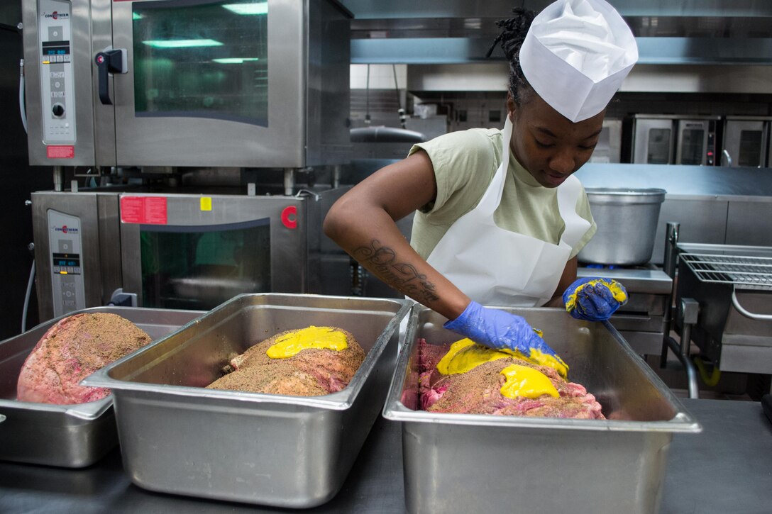 A Green Beret spreads mustard over steamship round roasts as she and others prepare a Thanksgiving dinner in the unit’s dining facility on Eglin Air Force Base, Fla., Nov. 23, 2015. U.S. Army photo by Maj. Thomas Cieslak