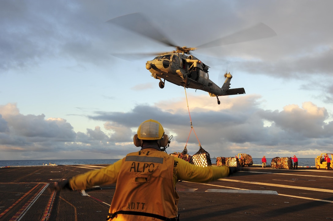 Navy Petty Officer 1st Class Manuel Arias directs an MH-60S Sea Hawk helicopter to lower its cargo onto the flight deck of the aircraft carrier USS Dwight D. Eisenhower during a replenishment at sea with the USNS Kanawha in the Atlantic Ocean, Nov. 29, 2015. Arias is an aviation boatswain’s mate. U.S. Navy photo by Petty Officer 3rd Class Taylor L. Jackson