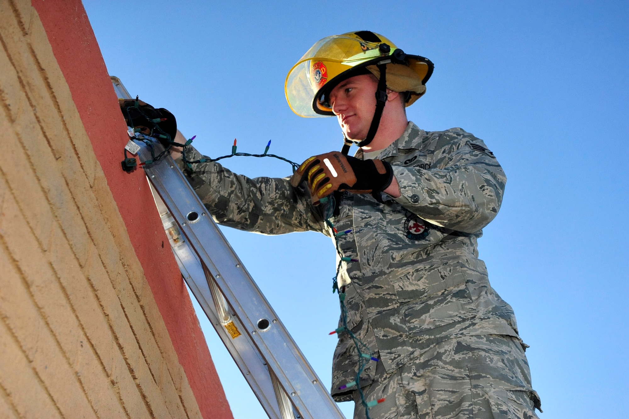 Senior Airman Ian Lucas, 56th Civil Engineer Squadron Fire Services driver operator, practices proper safety procedures while hanging Christmas lights Nov. 24, 2015 at Fire Station 361 at Luke Air Force Base, Ariz. When hanging Christmas lights ensure someone is holding the ladder at all times. (U.S. Air Force photo by Senior Airman Grace Lee)