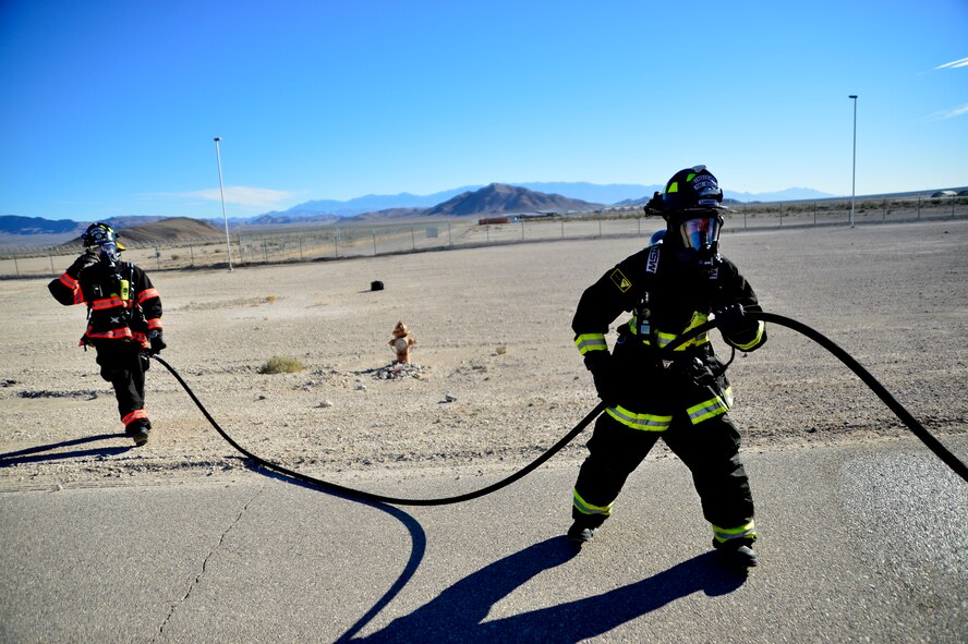 Carl, front, and Kevin, 99th Civil Engineering Squadron fire fighters, put a fire hose away after putting out a simulated munitions fire Nov. 24, 2015, at Creech Air Force Base, Nevada. The simulated munitions fire was part of a munitions storage area exercise to test the evacuation procedures for munitions personnel and firefighting and emergency medical technician procedures with fires around live ordnance. (U.S. Air Force photo by Airman 1st Class Christian Clausen/Released)