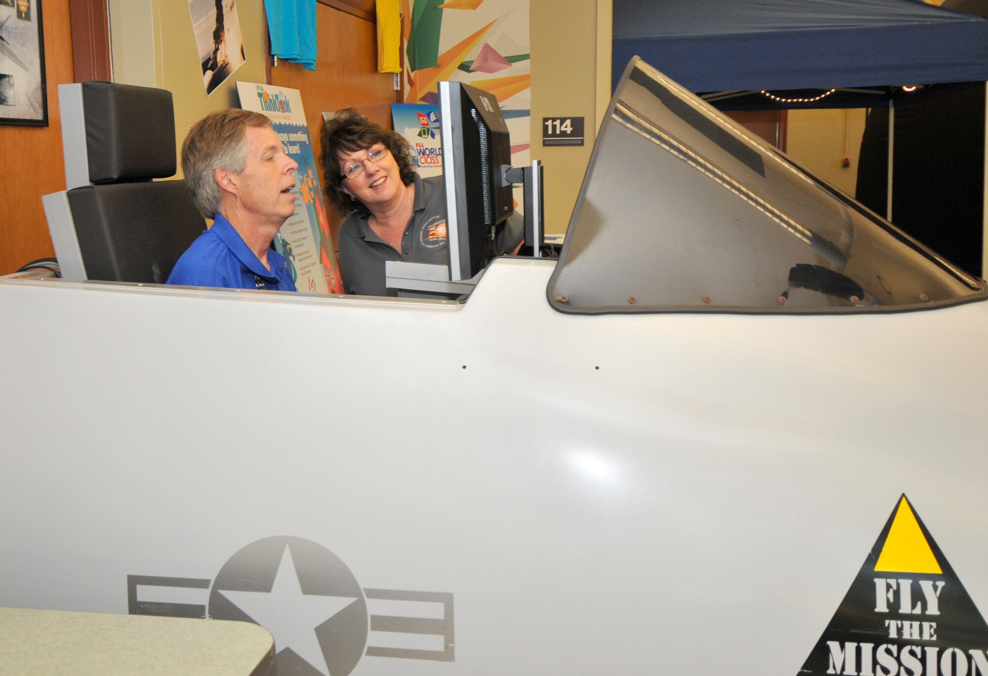 Carole Thomas watches AEDC STEM coordinator Jere Matty in the flight simulator used as part of the Fly to Learn program that enables students to fly virtual aircraft and study concepts such as energy and force.