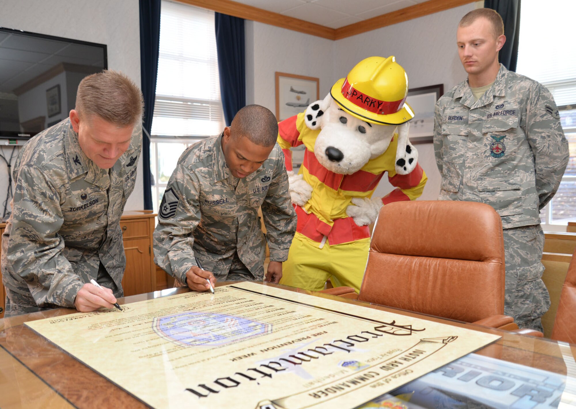 U.S. Air Force Col. Thomas D. Torkelson, left, 100th Air Refueling Wing commander, and Master Sgt. Shanton Russell, 100th Civil Engineer Squadron Fire Department deputy fire chief, sign the Fire Prevention Week Proclamation as Sparky the Fire Dog and Airman 1st Class William Burden, 100th CES Fire Department firefighter look on Sept. 30, 2015, to start off FPW events on RAF Mildenhall, England. Events include demonstrations at the BXtra, visits to the youth center and child development center with Sparky, reading with Sparky at the base library, and open house and a fire muster at the fire department. (U.S. Air Force photo by Karen Abeyasekere/Released)