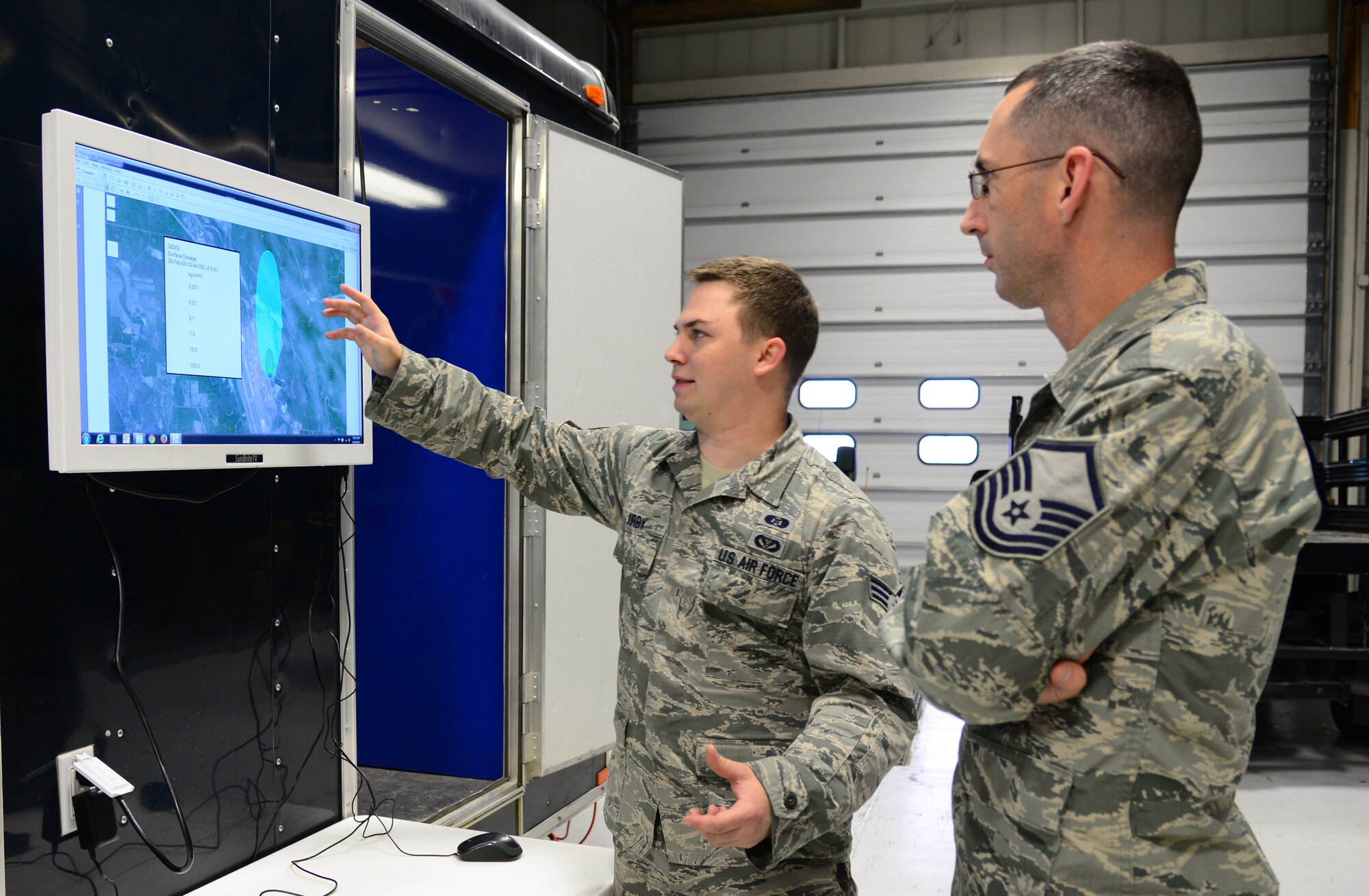 U.S. Air Force Senior Airman Sean Kirby, a 354th Civil Engineer Squadron emergency management journeyman, explains joint effects modeling to Master Sgt. Jason Blair, the 354th CES emergency management superintendent, Sep. 29, 2015, at Eielson Air Force Base, Alaska. The model on the screen shows a simulated chlorine plume and what areas could be affected. (U.S. Air Force photo by Airman 1st Class Cassandra Whitman/Released)