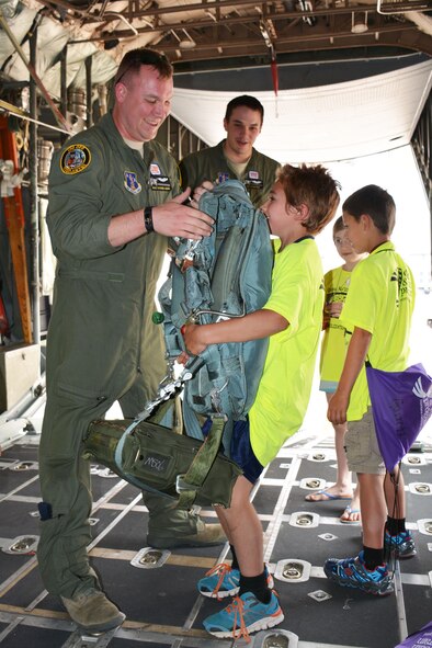 Montana Air National Guard C-130 Hercules Loadmaster Master Sgt. Steven Jager helps a young family member of a Montana National Guardsman feel the weight of a parachute during a tour of the transport aircraft. Eleven children of Guard families were participating in Kids Mobility Day at the 120th Airlift Wing in Great Falls, Mont., Aug. 20, 2015. (U.S. Air National Guard photo/Senior Master Sgt. Eric Peterson)