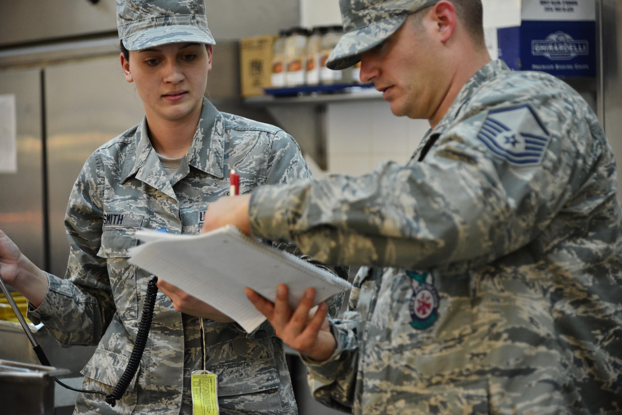 Senior Airman Leah Smith, 379th Expeditionary Medical Operations Support Squadron Bioenvironmental, overlooks as Master Sgt. Christopher Lance, 379th Expeditionary Civil Engineer Squadron Fire Department, writes down the corresponding air flow measurements for each section of a dining facility ventilation system September 30, 2015 at Al Udeid Air Base, Qatar. (U.S. Air Force photo/Staff Sgt. Alexandre Montes)  