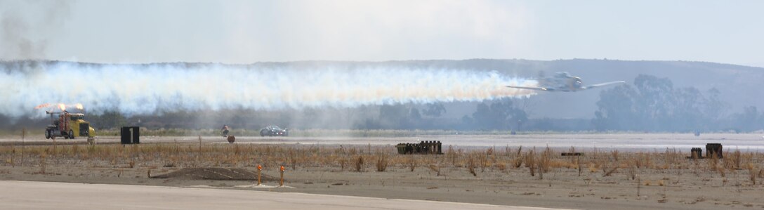 The jet-propelled Shockwave Jet Truck races an AT-6 Wardog during the 2015 MCAS Miramar Air Show aboard Marine Corps Air Station Miramar, California, Oct. 2. The annual air show features performances by both civilian and military aircraft as well as ground-based demonstrations and static displays. (U.S. Marine Corps photo by Sgt. Lillian Stephens/Released)