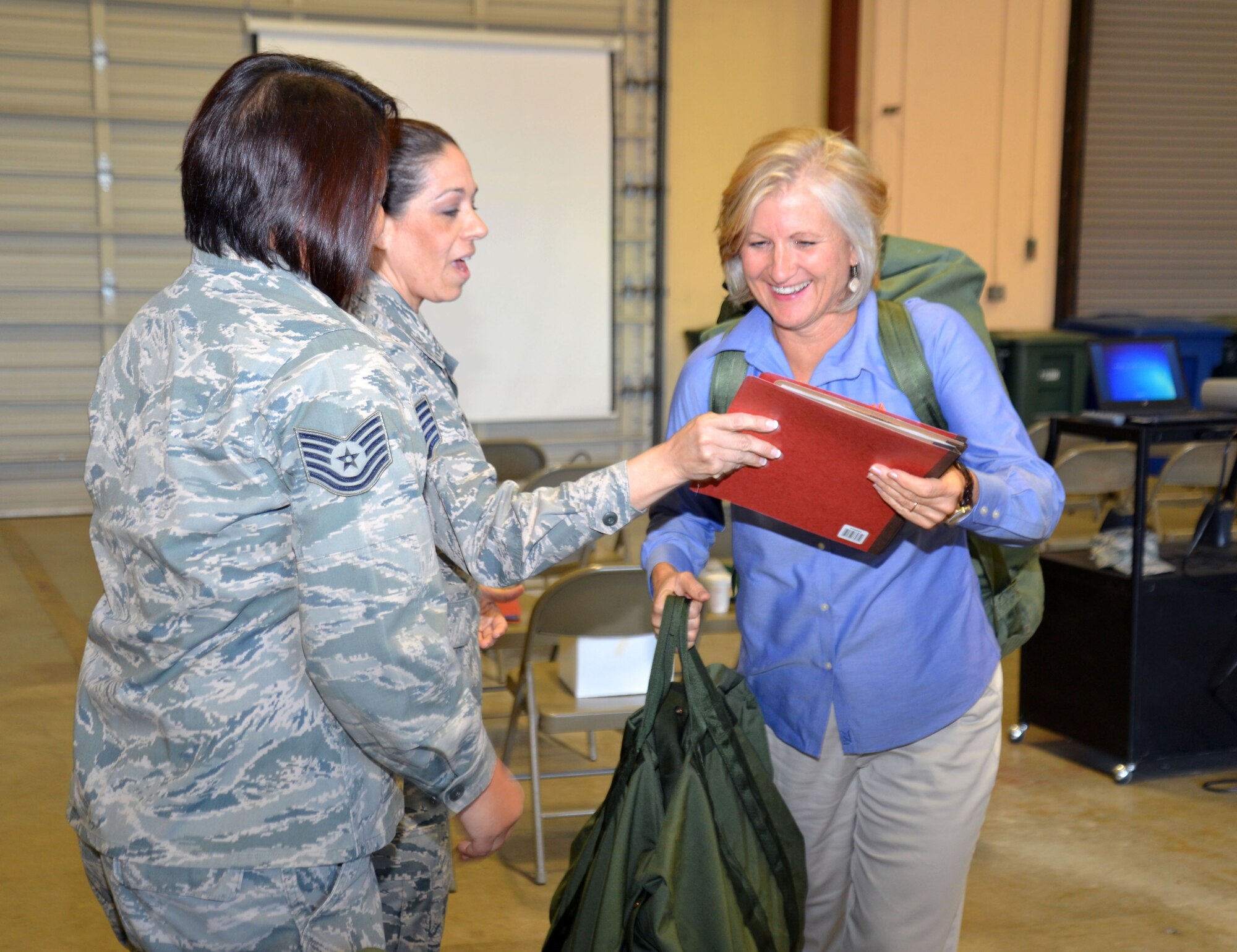 Tech. Sgts. Rosemarie Camacho (left) and Carmen Touchette, both of the 433rd Logistics Readiness Squadron, process Audrey Magnuson, University of Texas at San Antonio University Career Center director, through a mock deployment line Oct. 3, 2015 at Joint Base San Antonio-Lackland. The logistics readiness demonstration, which also included donning chemical gear, was part of a 433rd Airlift Wing Honorary Commander program tour of the 433rd Mission Support Group. (U.S. Air Force photo/Tech. Sgt. Lindsey Maurice)
