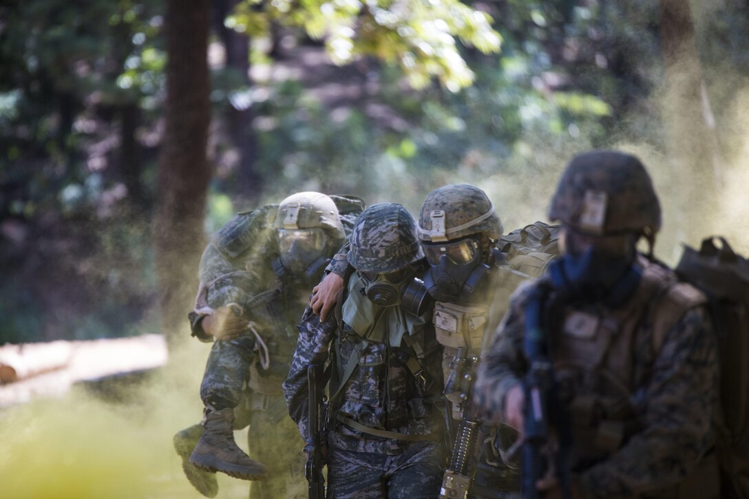 Republic of Korea Marine Lance Cpl. Jun Shin, center, supports a U.S. Marine moving to safety during a gas attack drill as part of Korean Marine Exchange Program 15-12 at Gunha-Rhi, Republic of Korea, Sept. 17, 2015. The drill was part of KMEP 15-12, an exercise that enhances the ROK and U.S. alliance, promotes stability on the Korean Peninsula and strengthens ROK and U.S. military capabilities and interoperability. Shin is with 2nd Company, 11th Battalion, 1st Regiment, 2nd Marine Division, ROK Headquarters Marine Corps. The U.S. Marines are with Fox Company, 2nd Battalion, 3rd Marine Regiment, currently supporting 3rd Marine Division under the unit deployment program.