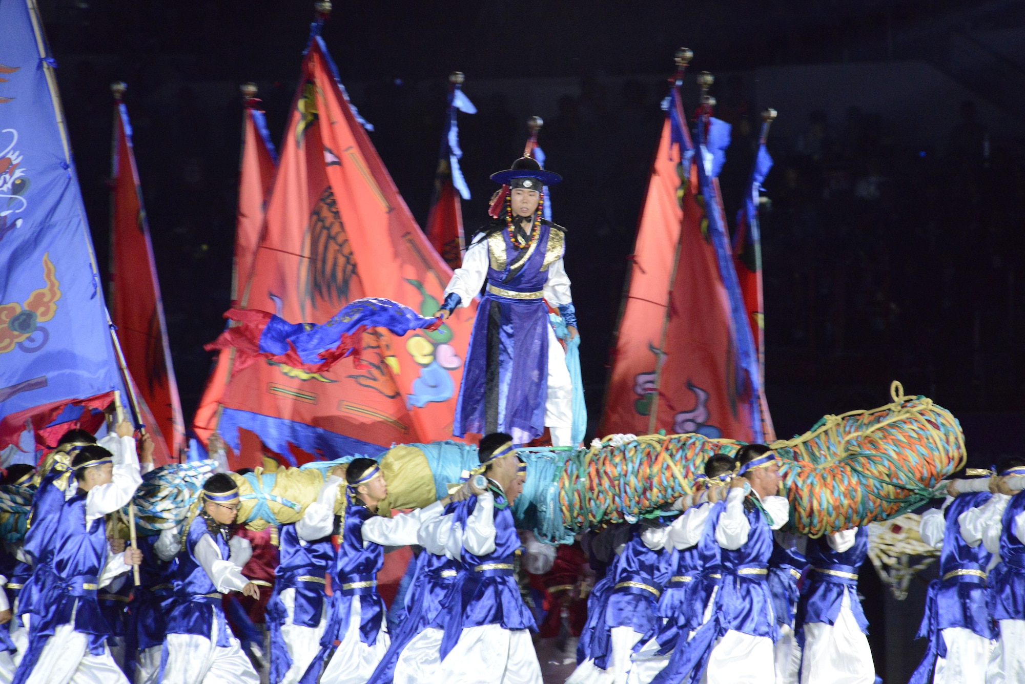 A scene of the opening ceremony of the CISM World Games depicts the traditional Korean game called Chajeon Nori. It involves teams of men carrying large log frames called dongchae. Atop each dongchae is a commander who directs his team to maneuver against the opposing team.