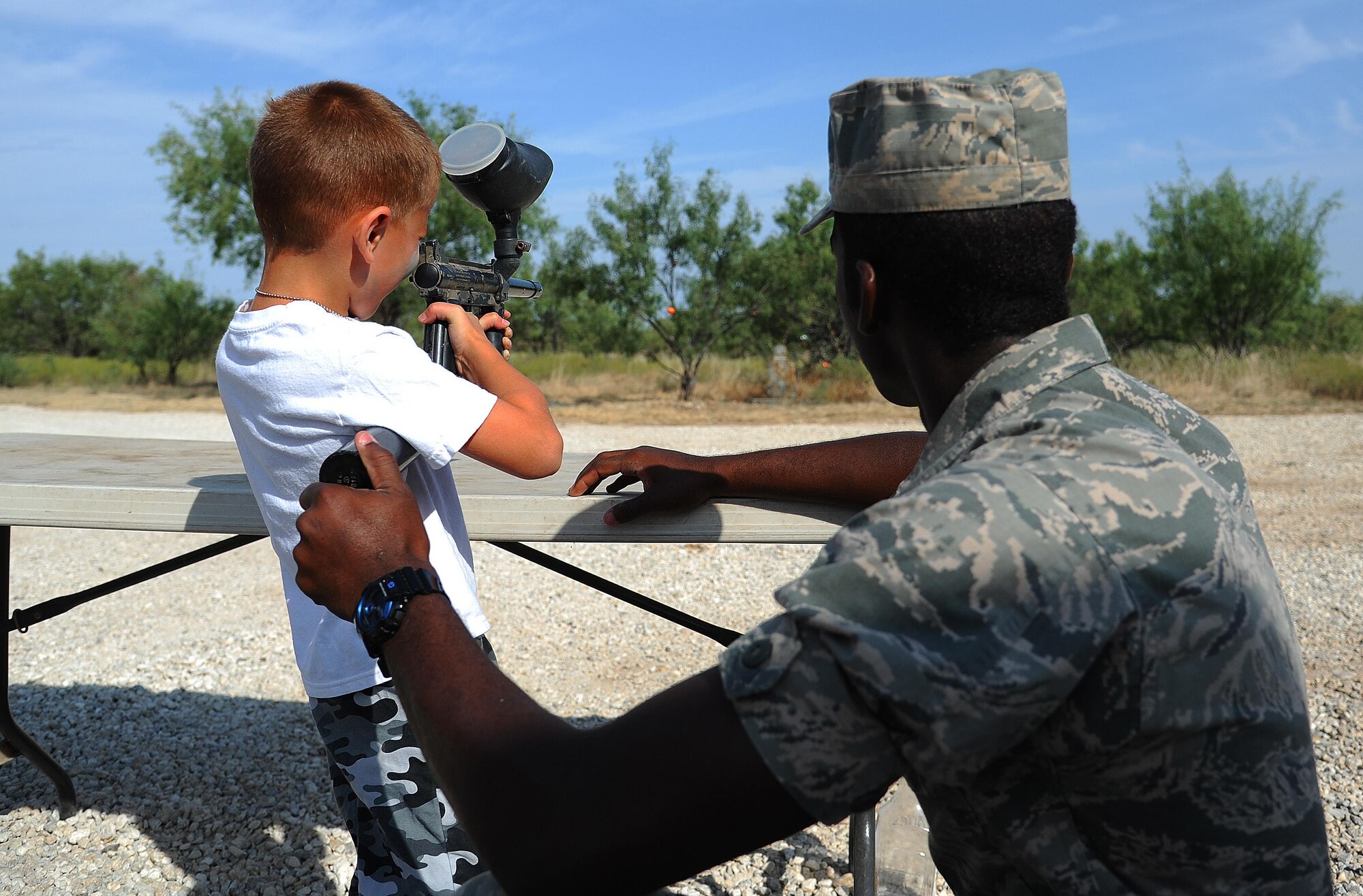 A dependent aims a paintball gun at a stone target with help from a volunteer during Operation K.I.D.S at Goodfellow Air Force Base, Texas, Oct. 3, 2015. Operation K.I.D.S gave children the opportunity to learn basic combat training and deployment exercises. (U.S. Air Force photo by Airman Caelynn Ferguson/Released)