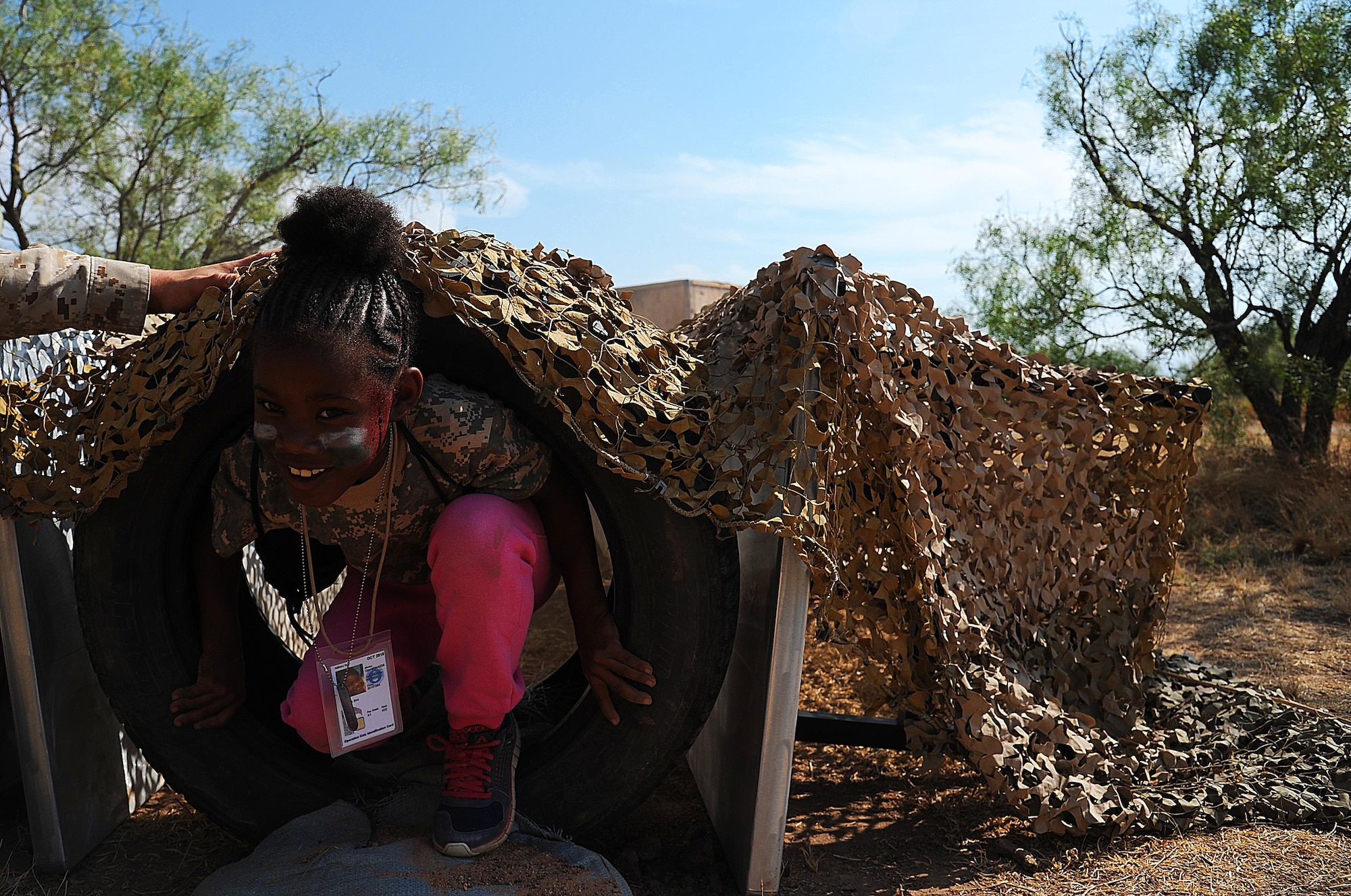 A dependent crawls through a camouflaged obstacle with the aid of a volunteer during Operation K.I.D.S at Goodfellow Air Force Base, Texas, Oct. 3, 2015. The children completed their final mission by clearing rooms, running through obstacles and attacking mock terrorists with foam batons. (U.S. Air Force photo by Airman Caelynn Ferguson/Released)
