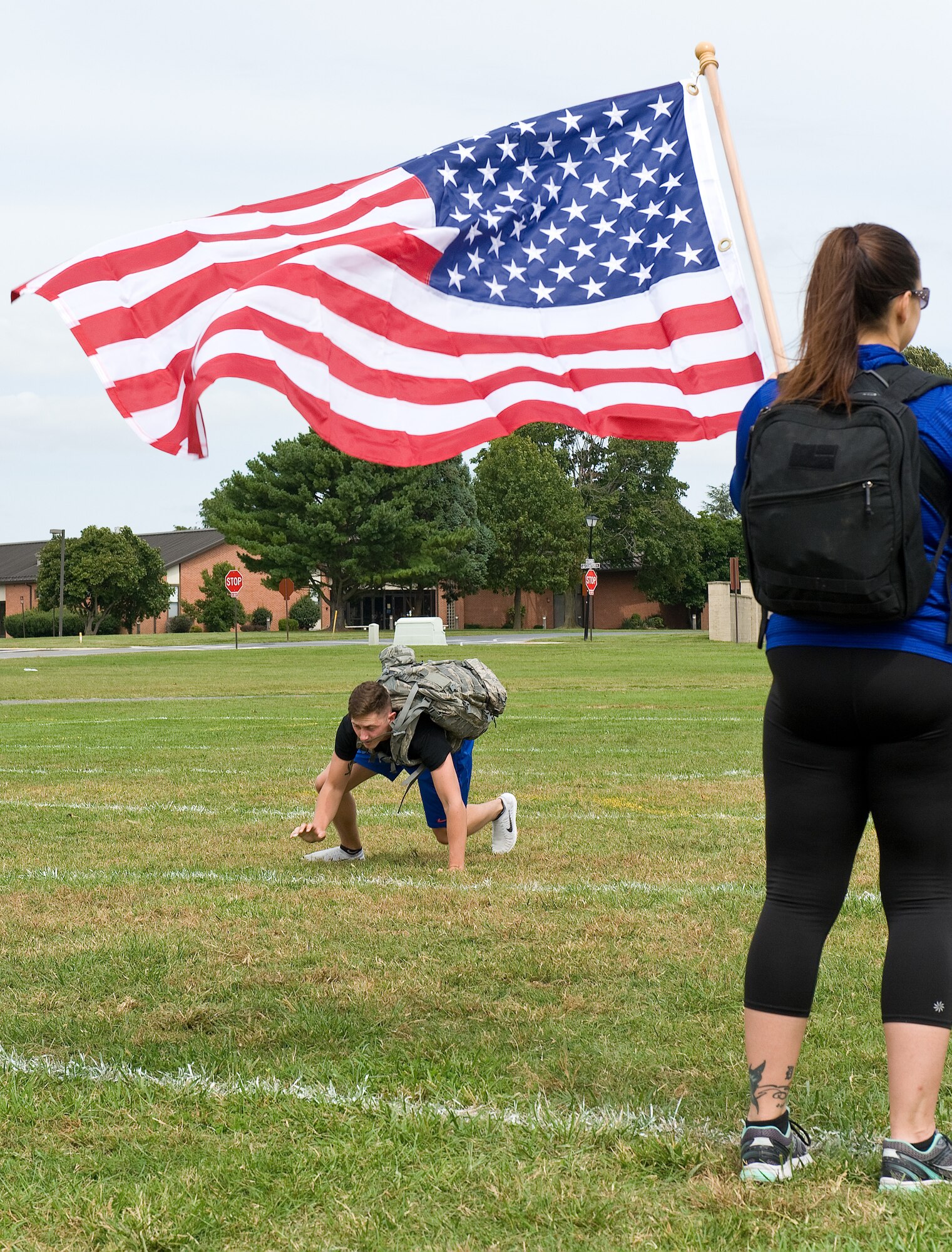Airman 1st Class Matthew Vidican, 436th Security Forces Squadron response force member, bear crawls during the GORUCK Light team cohesion challenge Sept. 25, 2015, on Dover Air Force Base, Del. Kristy Touchinsky, wife of Chris Stokes, GORUCK Light event cadre, holds the U.S. flag while Team Dover members participate in physical challenges. As a mandatory item for the GORUCK Light team, the flag was never allowed to touch the ground and was always at the front of the GORUCK Light formation over the 7.8-mile course. (U.S. Air Force photo/Roland Balik)