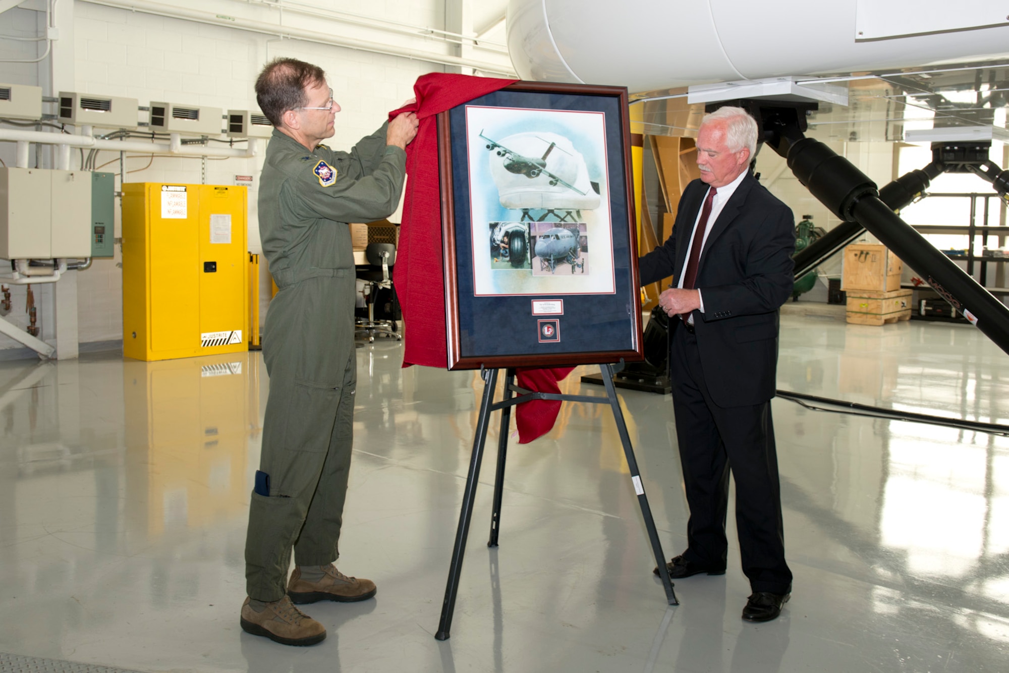 Col. Richard Robichaud, 167th Operations Group commander, assists Rodney Shrader, director of Air Force programs with L-3 Link Simulation and Training, with the unveiling of a framed print presented to the 167th Airlift Wing during the C-17 simulator training facility ribbon cutting ceremony, Sept. 24.(U.S. Air National Guard photo by Master Sgt. Emily Beightol-Deyerle/Released)