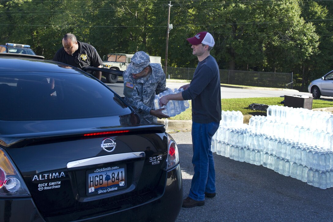 Soldiers work alongside local law enforcement and volunteers to distribute drinking water to residents affected by heavy rainfall caused by Hurricane Joaquin at the Lower Richland High School, Columbia, S.C., Oct. 6, 2015.  
