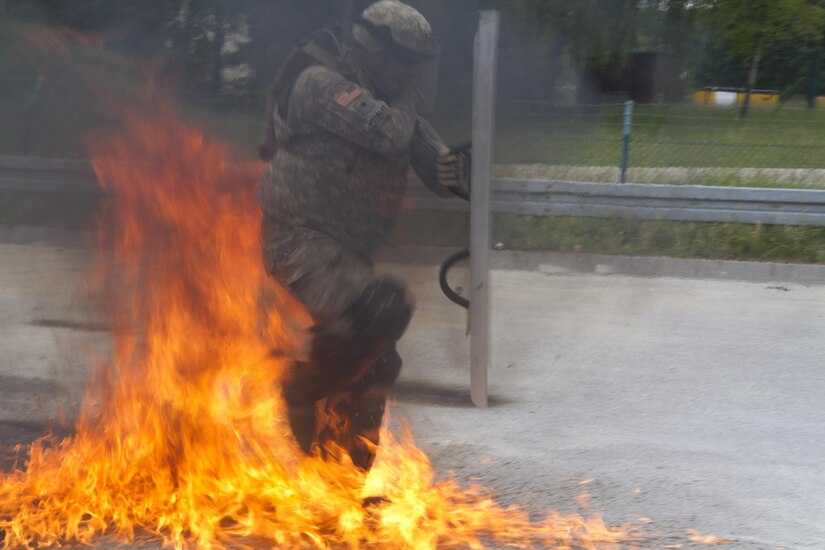 Spc. Michael Morales with the 1st Battalion, 252nd Armor Regiment’s Alpha Company, maneuvers his way through flames of a broken Molotov cocktail thrown by a member of the Portuguese army military police during fire phobia training June 16 in Hohenfels, Germany. This exercise is designed to help peacekeeping troops actively go through the steps of what to do when Molotov cocktails are encountered during crowd and riot control.