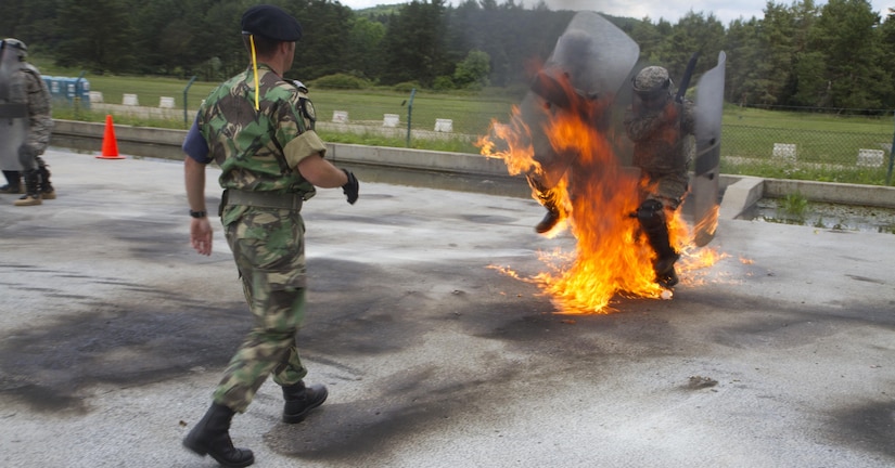 U.S. Soldiers with the 1st Battalion, 252nd Armor Regiment, maneuver their way through flames of a broken Molotov cocktail thrown by a member of the Portuguese army military police during fire phobia training June 16 in Hohenfels, Germany. This exercise is designed to help peacekeeping troops actively go through the steps of what to do when Molotov cocktails are encountered during crowd and riot control.