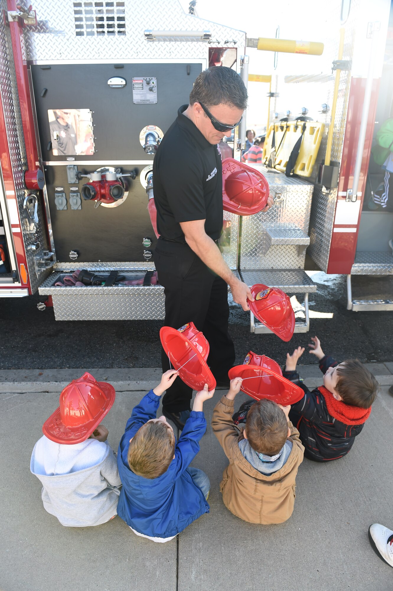 David Herman, Buckley Fire Department assistant fire chief, hands children from the Crested Butte Child Development Center plastic fire helmets Oct. 7, 2015, on Buckley Air Force Base, Colo. The fire department visited both CDCs on base to spread the word about Fire Prevention Week. For the visit, the children got to meet Sparky the Fire Dog, look at fire trucks, and take home coloring books. (U.S. Air Force photo by Airman 1st Class Samantha Meadors/Released)