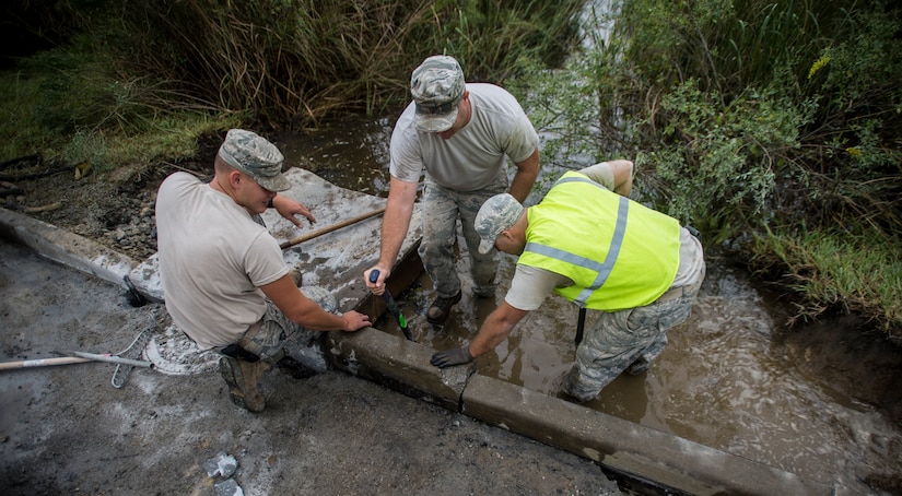 (Left to right) Airman 1st Class Daniel Wade, 628th Civil Engineer Squadron heavy equipment operator, Tech. Sgt. Aaron Wade, 628th CES NCOIC Weapons Station Horizontal Section and Staff Sgt. Devin Kennedy, 628th CES heavy equipment operator all work to fix road damage caused by floods from heavy rains Oct. 6, 2015, on a road on Joint Base Charleston – Weapons Station, S.C. While hurricane Joaquin did not make landfall on the east coast, a constant flow of heavy rain caused flooding throughout the Carolinas. The 628th CES quickly accessed the damage and took action to fix and restore base assets. (U.S. Air Force photo/Airman 1st Class Clayton Cupit)