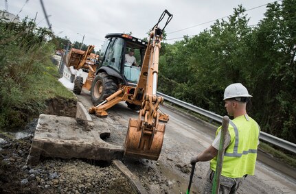 Staff Sgt. Devin Kennedy, 628th Civil Engineer Squadron heavy equipment operator, watches as Tech. Sgt. Aaron Wade, 628th CES NCOIC Weapons Station Horizontal Section, puts a sewer cover into place Oct. 6, 2015, on a road on Joint Base Charleston – Weapons Station, S.C. While hurricane Joaquin did not make landfall on the east coast, a constant flow of heavy rain caused flooding throughout the Carolinas. The 628th CES quickly accessed the damage and took action to fix and restore base assets. (U.S. Air Force photo/Airman 1st Class Clayton Cupit)