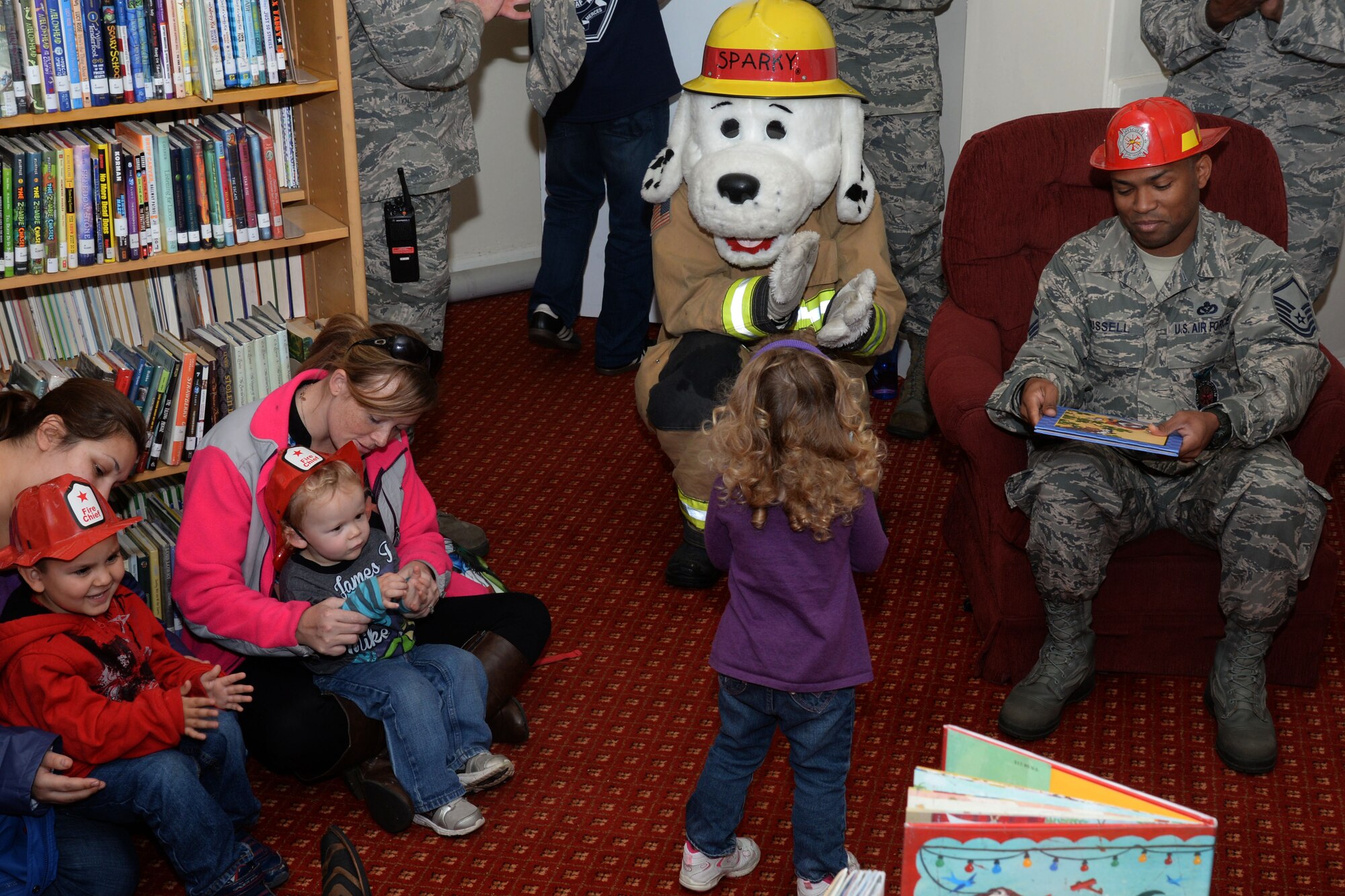 U.S. Air Force Master Sgt. Shanton Russell, 100th Civil Engineer Squadron Fire Department deputy fire chief, right, reads fire safety themed books to families and friends, Oct. 7, 2015, at the base library on RAF Mildenhall, England, as Sparky the Fire Dog claps along with his young fans. Fire Prevention Week’s theme this year is “Hear the beep where you sleep; every bedroom needs a working smoke detector.” (U.S. Air Force photo by Airman 1st Class Justine Rho/Released)  