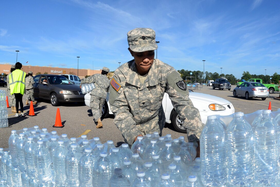 Army National Guardsmen work with local law enforcement and volunteers to distribute drinking water to residents affected by heavy rainfall caused by Hurricane Joaquin at the Lower Richland High School, Columbia, S.C., Oct. 6, 2015. South Carolina Air National Guard photo by Airman 1st Class Ashleigh S. Pavelek 