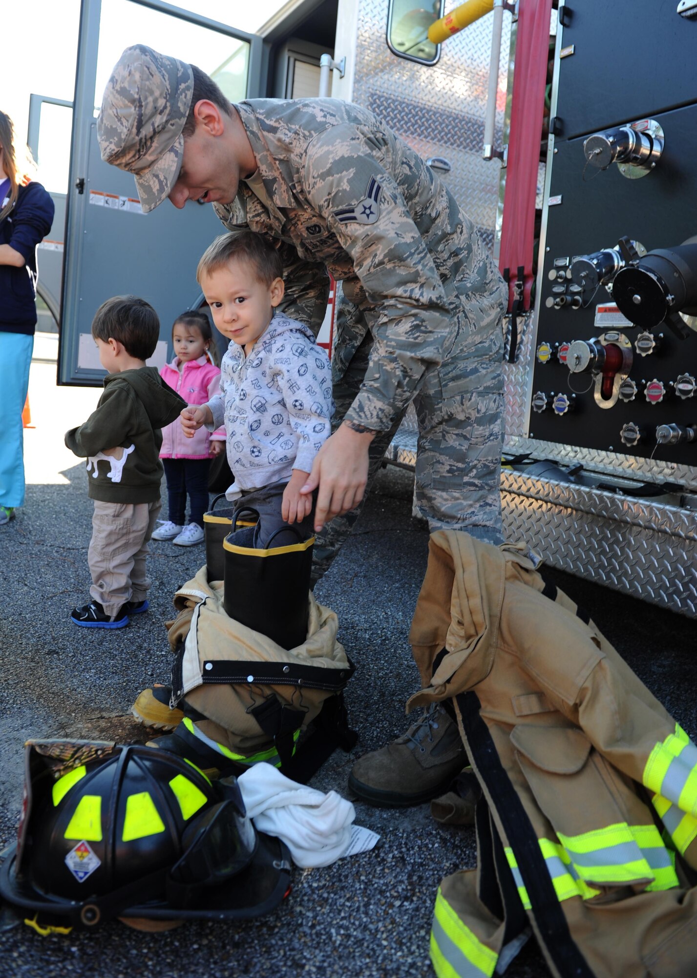 Airman 1st Class Erik McAskill, 81st Infrastructure Division firefighter driver operator, assists Brenton Williams, son of Maj. Jonathan Williams, 336th Training Squadron director of operations, as he fits into firefighter gear during a Fire Prevention Week visit, Oct. 6, 2015, Keesler Air Force Base, Miss. Throughout  the week the Keesler Fire Department is conducting random fire drills, touring various facilities with Sparky the Fire Dog, passing out fire safety handouts and fire hats for children and providing stove and fire extinguisher demonstrations. The week–long event will conclude with an open house at the fire station 10 a.m. to 2 p.m. Oct. 10.