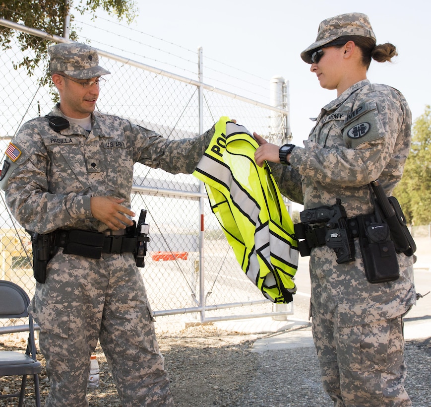U.S. Army Spc. Juan Padilla, a military police officer with the 382nd Military Police Detachment from San Diego, provides a police safety vest to Spc. Josephine Ixta, a 382nd MP at an entry control point at Fort Hunter Liggett, Calif., Aug. 1.  Padilla, a San Diego native and Ixta, a Los Angeles native, worked with Fort Hunter Liggett police to maintain law and order, and force protection during their annual training, July 26-Aug. 10. The 382nd supported WAREX 91-15, “Operation Caucasus Restore.” WAREX 91-15 prepares Reserve and National Guard units with real world and scenario based training, as well as basic Soldier skills during the exercise. (Photo by U.S. Army Staff Sgt. Nazly Confesor, 200th MP Command Public Affairs/Released)