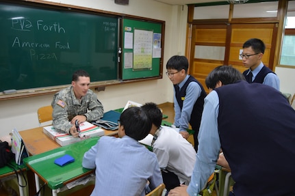 Pvt. Brandon Forth, a Patriot launching station enhanced operator/maintainer assigned to Headquarters and Headquarters Battery, 6th Battalion, 52nd Air Defense Artillery Regiment, shares his typical experience of American culture during a visit with South Korean students of Kwonsun Middle School Sept. 23, 2015. Forth is one of 15 Soldiers that took part in the American culture and conversational English lesson for the school.