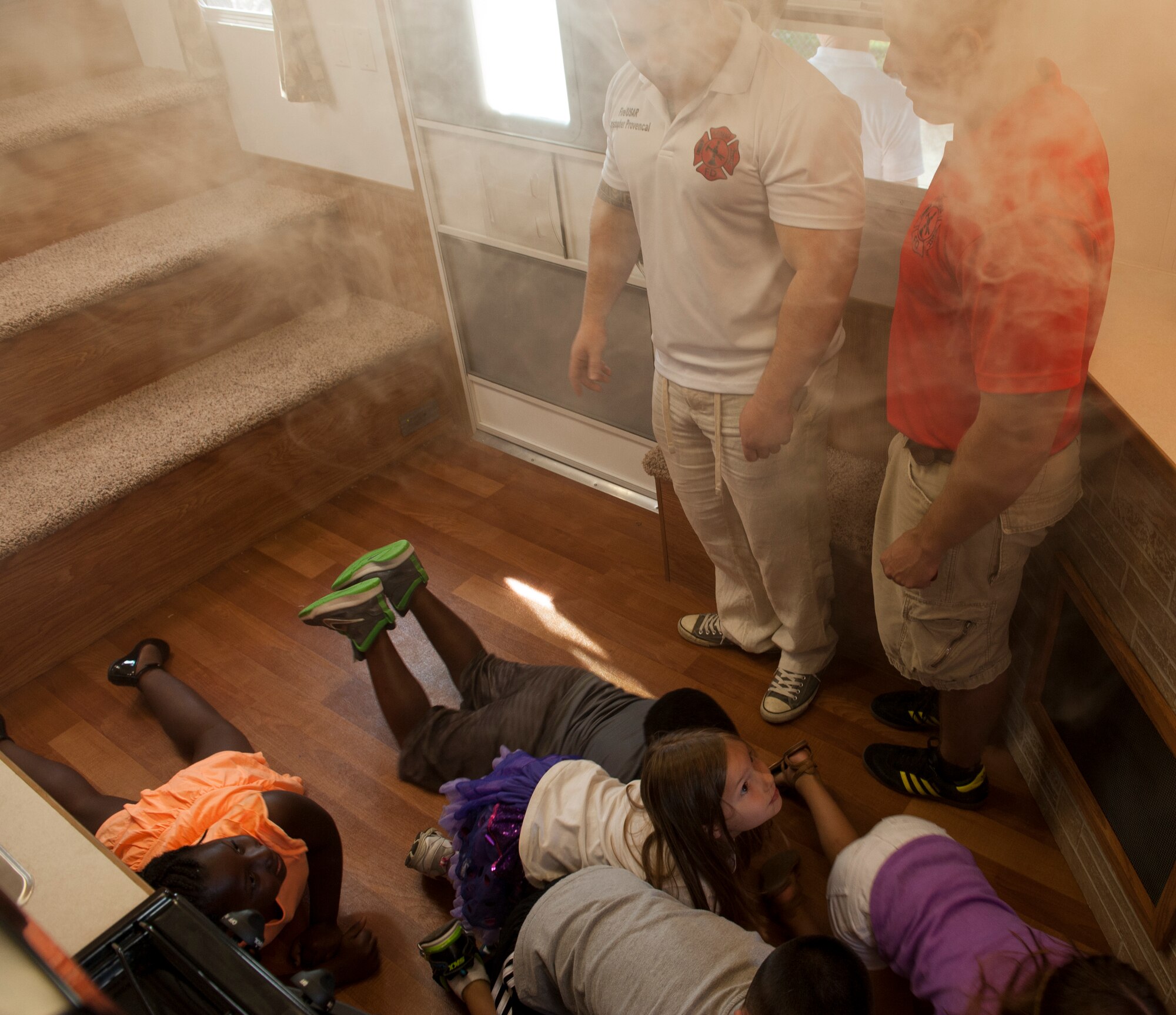 U.S. Air Force firefighters from the 18th Civil Engineer Squadron, Tech. Sgt. Christopher Provencal and Staff Sgt. Cory Challenger, direct Kadena Elementary School children on what to do when they see smoke and hear a smoke alarm as part of Fire Prevention Week Oct. 7, 2015, on Kadena Air Base, Japan. The Fire Department pumped artificial smoke into a trailer to simulate a fire in order to educate students on fire evacuation procedures. (U.S. Air Force photo by Airman 1st Class Corey M. Pettis)