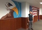 DLA Distribution Puget Sound, Wash., quality assurance supervisor Rosauro Aldana stands between the two of the three hand painted murals he created in the organization’s command suite.